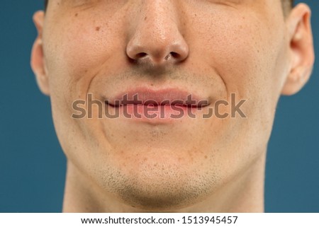 Caucasian young man's close up shot on blue studio background. Beautiful model with well-kept skin. Concept of human emotions, facial expression, sales, ad, male beauty and healthcare. Lips and cheeks