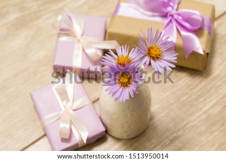 Purple spring flowers in a white vase on a wooden table. Gift box wrapped in craft paper with ribbon