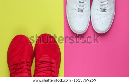 Two pairs of sneakers on a neon color background. White and red shoes. Top view