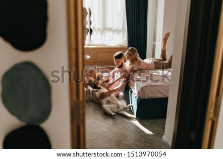 Weekend photo of couple playing with Labrador in sunny bedroom. Guy and girl are stroking belly of big dog