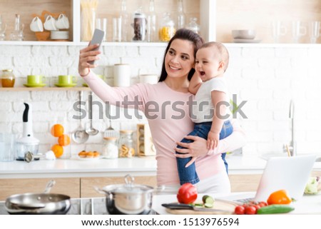 Kitchen selfie. Millennial mother taking selfie on cellphone, smiling at camera, free space