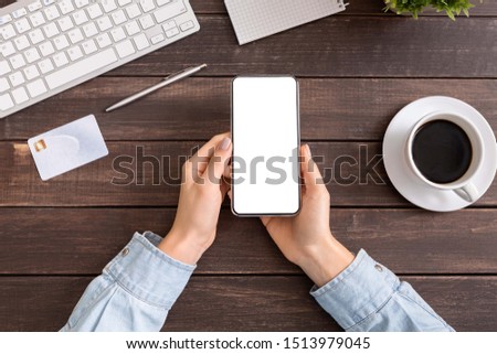 Woman hands holding smartphone with blank white screen in office, top view, copy space