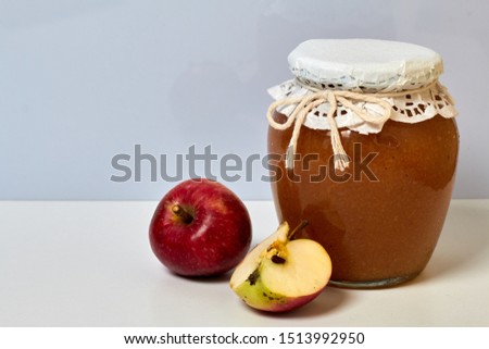 Homemade seasonal preparations. Beautifully packaged jars of apple jam. Covered with paper and tied with a cord. Nearby are fresh apples.