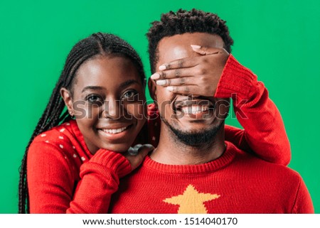 African American woman in red sweater covering eyes with hand to man isolated on green