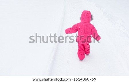Toddler child wearing pink fuchsia snowsuit walking in snow storm weather.  Royalty-Free Stock Photo #1514060759