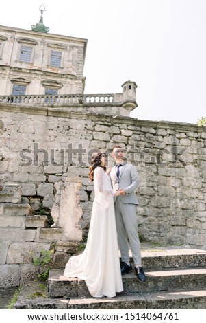 Beautiful fairytale newlywed Asian couple holding hands and kissing near old medieval castle