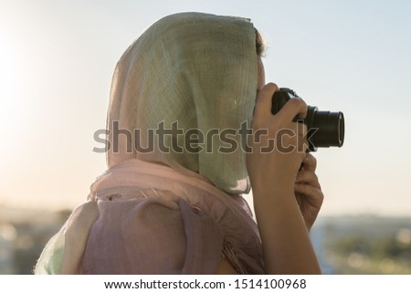 Arab Woman Photographer in a scarf taking picture using Camera on the sunset background. Halal travel concept 