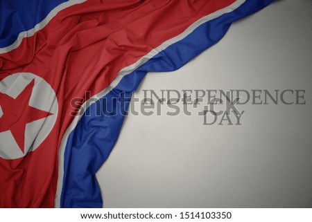 waving colorful national flag of north korea on a gray background with text independence day. concept
