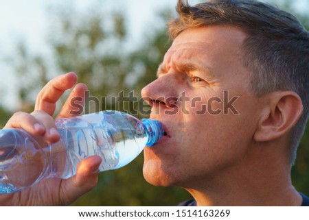 Young handsome man holding a bottle with still pure water and drinking. He slaking her thirst in hot summer day. Healthy lifestyle concepts. High resolution photography
