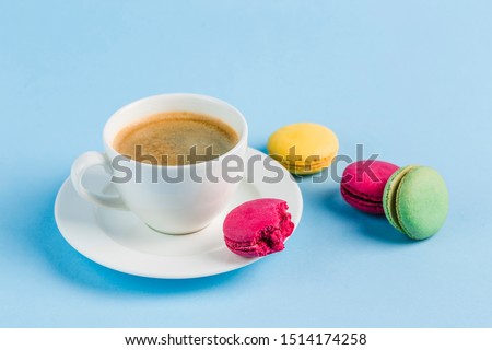 Colorful macaroons with a white Cup of coffee on a blue background, close-up, Flatley with copy space. Dessert with melon, lemon and raspberry flavor. Art