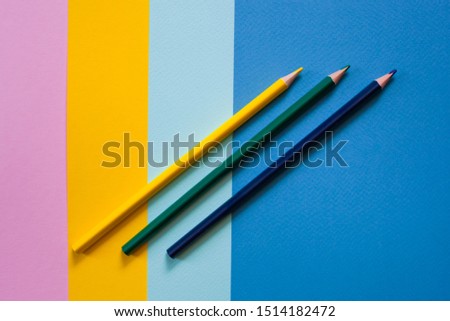 three colored pencils on a colored background of paper lie obliquely, flat lay
