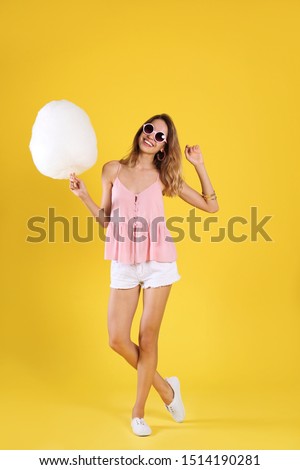 Happy young woman with cotton candy on yellow background