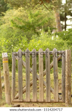 Rustic wooden plank fence gate closed with a worn trail sign on one of its posts in the countryside on a background of lush forest.