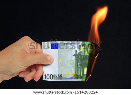Hand holding a  100 euros bank note burning conceptual picture on black background