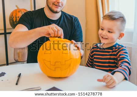 young father with toddler son making jack pumpkin head for halloween holiday