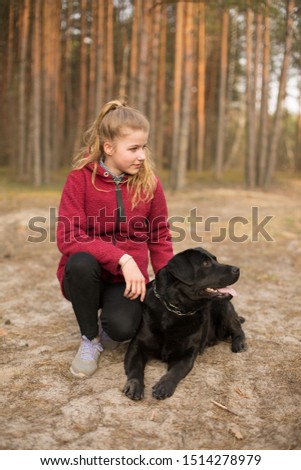 girl walking with dog in forest. beautiful girl sitting with dog on a walk. black labrador, woman in red coat
