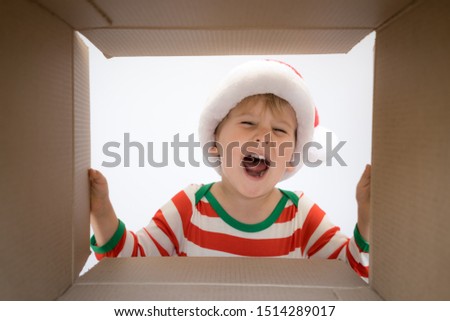 Happy child looking into the box. Funny surprised baby boy unpack Christmas gift box. Xmas holiday concept. Low angle view. 