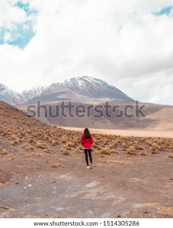 Tourist Woman with ramatic mountain landscape. Pretty wake lake landscape with mountain background. Mountain range view, shot in Salt Flats of Uyuni, Bolivia. Copy space, blue sky and green foreground