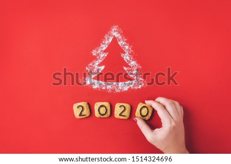 Flour Silhouette Christmas Tree with cookies digits 2020 on red background with women hand. Delicious bakery sweet confectionery Christmas card. Idea of merry new year xmas 2020 holiday