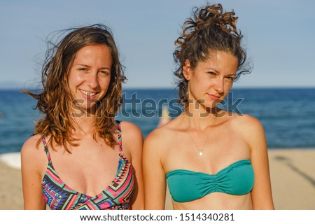 Portrait of two young women female girls friends or sisters in sunny day wearing bikini swim suit in front of the sea