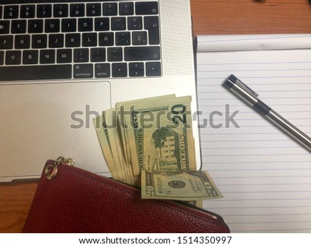 Computer and money with a red lady's wallet and a pen. Spanish keyboard.