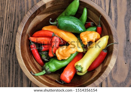 Close-up picture of a variety of colorful peppers in a wooden bowl on a wooden surface
