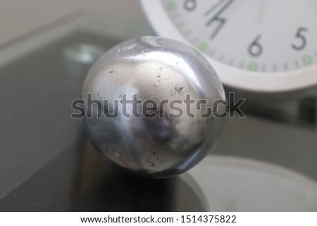 Aluminum foil ball on glass table with clock in background 