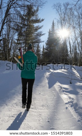 A young woman heads out out to a trail carrying her cross country ski equipment.