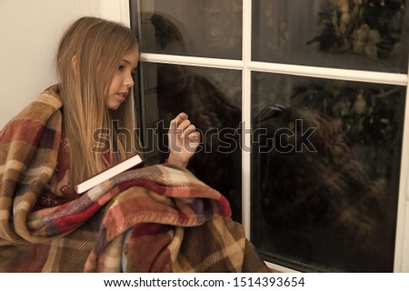 Christmas story time. Small child read book on Christmas eve. Small reader wrapped in plaid sit on window sill. Small girl enjoy reading Christmas book. Childrens picture book. Magic xmas spirit.
