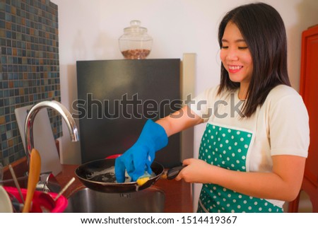 natural lifestyle portrait of young beautiful and happy Asian Chinese woman in apron and rubber glove washing dishes and pan smiling cheerful in relaxed housework and domestic chores concept