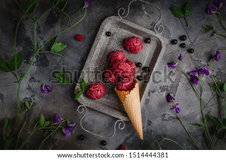berry ice cream scoops in single waffle cone on vintage metal tray with fresh berries and flowers, top view