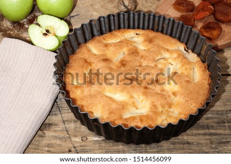 Charlotte apple pie on a wooden table with green apples in iron form