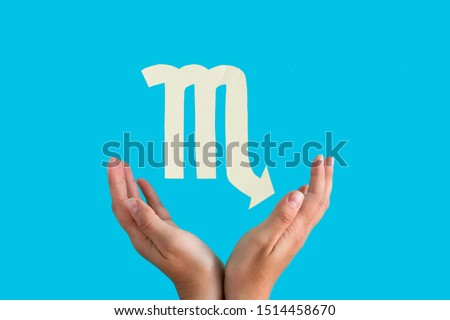 Scorpio astrological sign hanging over female hands on blue background, horoscope forecast concept