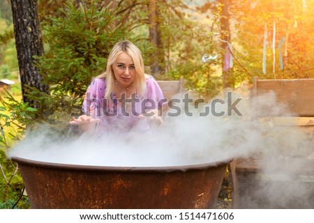 A young beautiful girl, a blonde witch is preparing a potion in a large cauldron on the eve of Halloween or the worshiping devil bringing in priesthood. Feminine witchcraft and influence on men.
