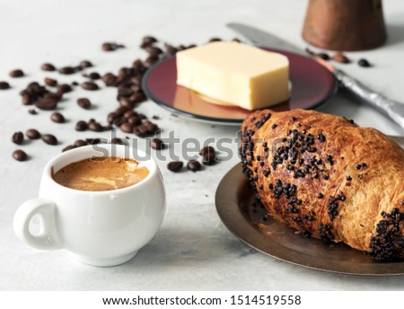 White coffee cup with espresso and croissant. Nearby are fresh coffee beans, butter and cezve. Located on a gray background. Close-up.