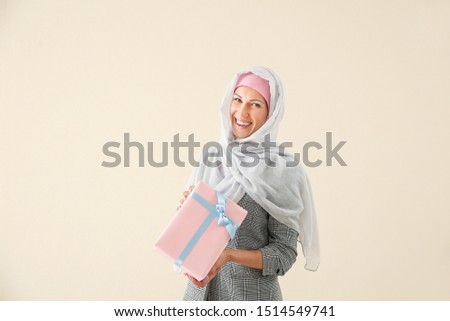 Beautiful young Muslim woman with gift on light background