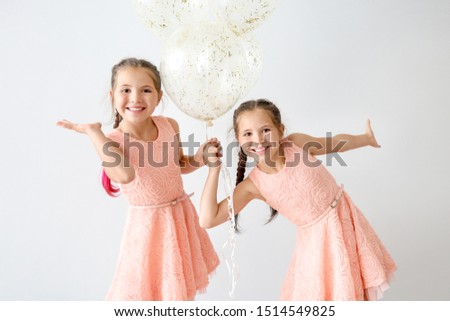 Portrait of happy twin girls with air balloons on light background