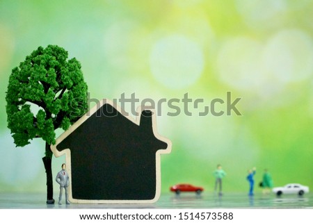 Miniature business man stand near black house wood board and tree on green bokeh background. Success of your life. Investment, business, property, saving concept. Copy space.