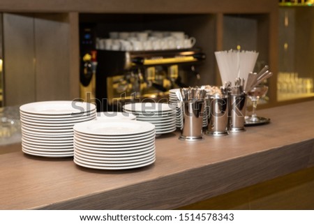 Bar counter with clean dishes close up. Barroom in restaurant, ready for work. Cafe background. Kitchen utensils, cookware (cups, a stack of plates, saucers, spoons, a teapot) on bar in cafe Royalty-Free Stock Photo #1514578343