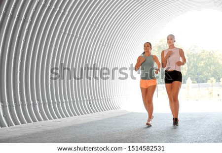 fitness, sport and healthy lifestyle concept - young women or female friends with earphones running outdoors