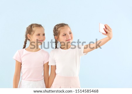 Portrait of twin girls taking selfie on color background