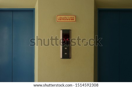 Closeup elevator button panel with LED display, above it is rectangular sign read in case of fire, do not use elevator in both Thai and English languages.   