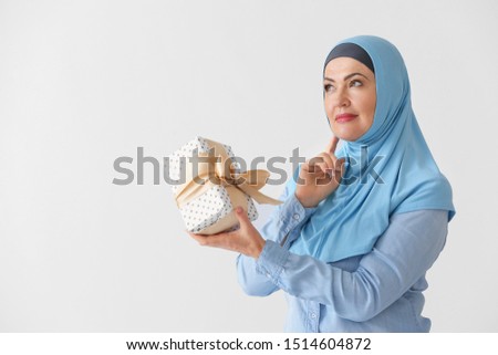 Beautiful mature Muslim woman with gift box on light background