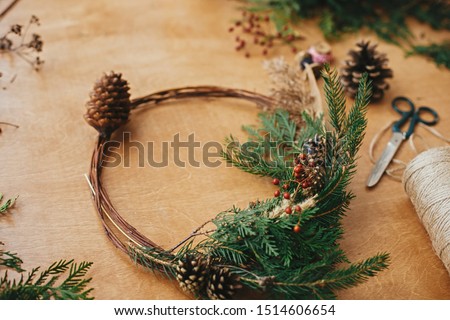 Rustic Christmas wreath. Creative christmas wreath with fir branches, berries, pine cones and herbs with scissors and thread on rural wooden table. Happy holidays. Workshop