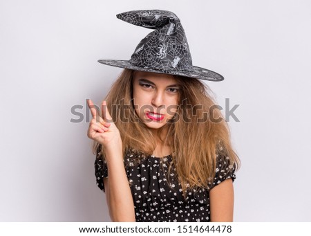 Happy halloween concept. Funny Teen girl in witch black hat posing on grey background. Cheering young teenager in witch halloween costume, looking at camera.
