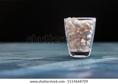 White pills in a glass on wooded table.