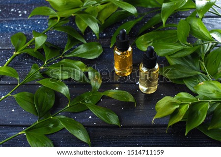 two jars with a dropper and yellow oil on a background of a space board with green fresh leaves