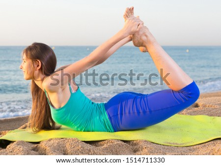 Female 20-25 years old is practicing stretching  in white T-shirt on the beach near sea.