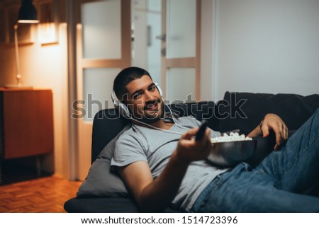 handsome young man relaxed on sofa at his home watching television and eating popcorn Royalty-Free Stock Photo #1514723396