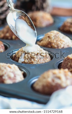 Fresh from the oven, homemade pumpkin muffins with streusel with spoon pouring icing over them. Selective focus on center muffin with extreme blurred foreground and background.